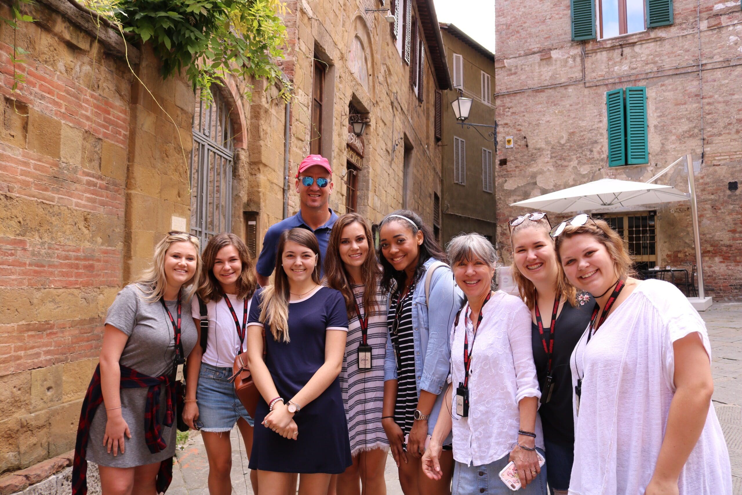 A large group of students crowds together with older tan brick buildings surrounding them.