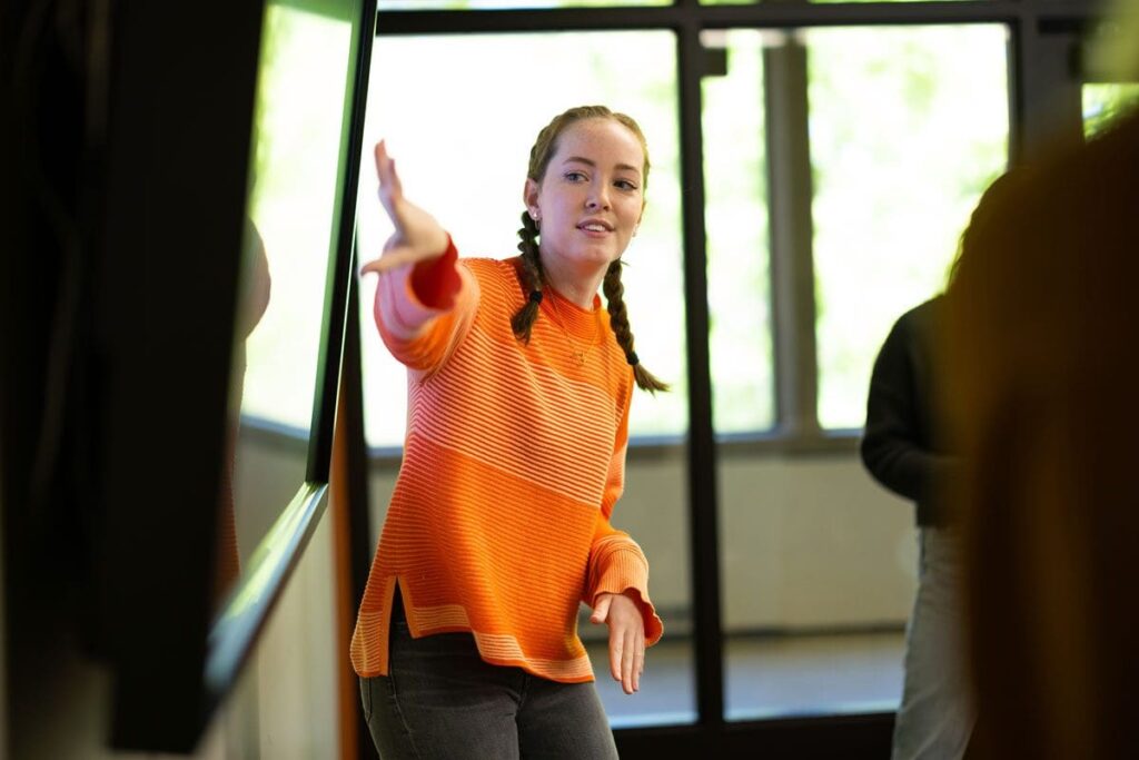 A student gestures toward a screen for a presentation in class.