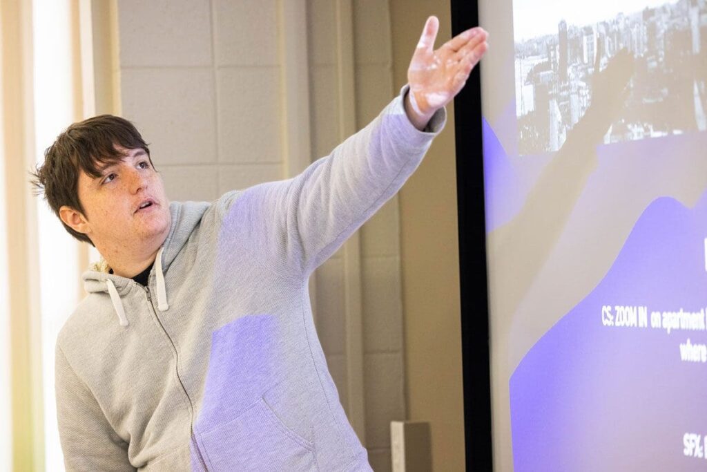 A student gestures to a projection screen during a class presentation.