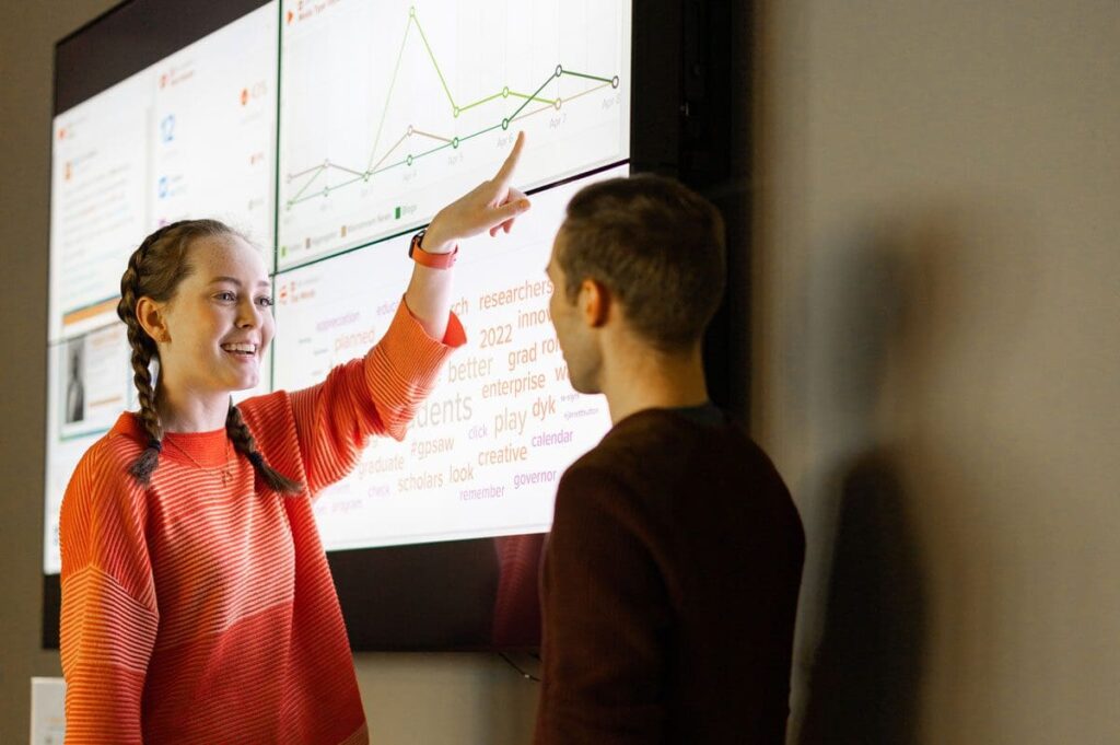 A student points to a screen with social media analytics on it.